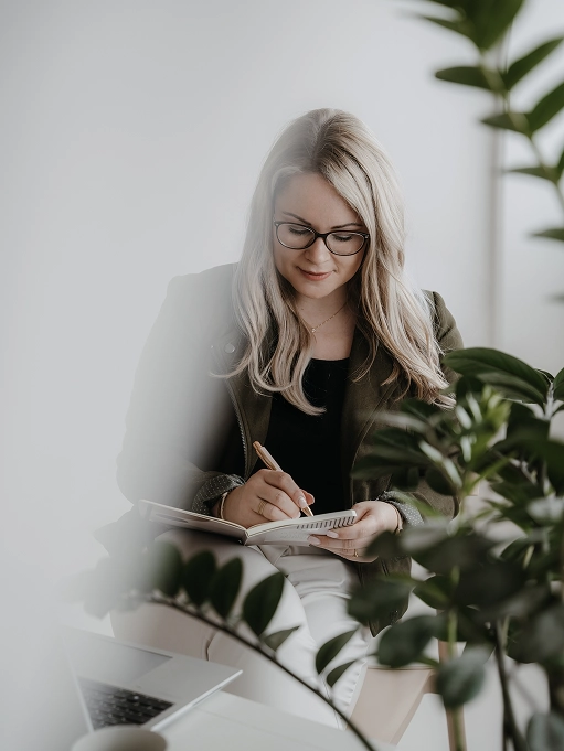 Professionelles Portrait von Berthilde Bittner beim Schreiben in einem Notizbuch, modernes Arbeitsumfeld mit Laptop und Pflanzen – Unternehmerberatung Regensburg, Kehlheim, Mainburg, Ingolstadt, Abendsberg, Schierling Beblick Coaching, Training & Beratung.