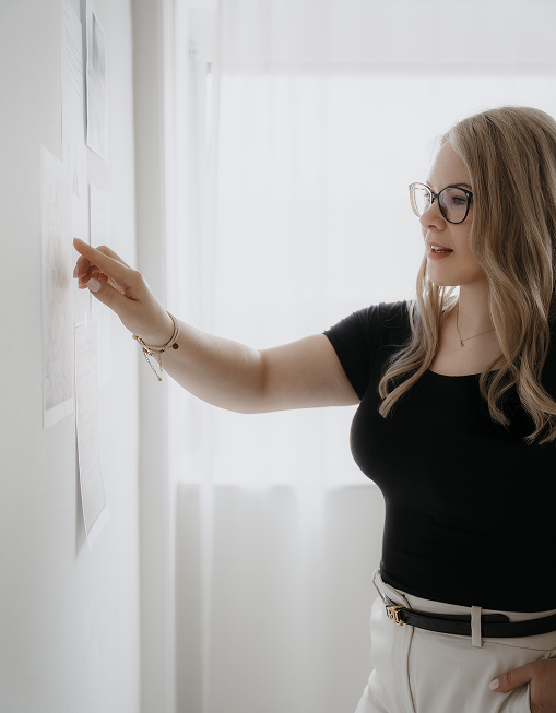 Szene mit Berthilde Bittner, die fokussiert an einer Wand mit ausgedruckten Unterlagen arbeitet, lichtdurchfluteter Raum, moderne Arbeitsweise – Leadership Coaching Niederbayern, Beblick Coaching, Training & Beratung für Unternehmer und Führungskräfte. Region Niederbayern, Regensburg, Abendsberg, Schierling, Mainburg, Kehlheim, Ingolstadt, Wolnzach.
