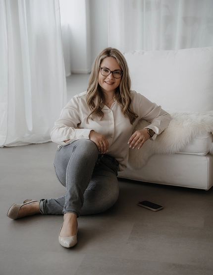 Professionelles Portrait von Berthilde Bittner, Beblick Coaching, sitzend leger am Boden in einem hellen Raum mit Sofa und Vorhängen, modern und nahbar – Unternehmer Coaching Schierling für Führungskräfte und Geschäftsführer.