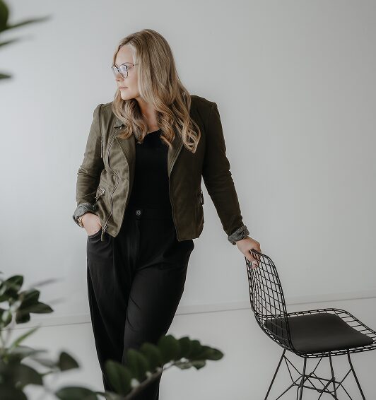 Portrait von Berthilde Bittner in modernem Business-Setting mit weißer Wand und Pflanzen, steht locker an einem Stuhl, wirkt reflektiert – Unternehmerberatung, Coaching, Training und Beratung aus Niederbayern, Beblick Coaching, Training & Beratung.